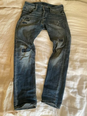 Blå slitna slim jean - Säljer ett par blå slim jeans med slitningar på benen. Jeansen har en klassisk femficksmodell, låg midja och är tillverkade i denim med stretch. Perfekta för en avslappnad och trendig look. De har även några gul på baksidan som man kan se på sista bilden men annars inget fel på dem