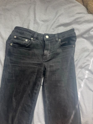 Svarta jeans med fickdetaljer - Säljer ett par svarta jeans med raka ben och coola fickdetaljer bak med silverknappar. Klassisk femficksmodell framtill och knappgylf. Jeansen har en snygg tvättad look och passar perfekt till streetwear eller casual outfits.