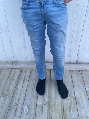 Ljusblå slim fit jeans ifrån nudie jeans - W27 L30 Säljer ett par ljusblå slim fit jeans med klassisk femficksdesign och dragkedja. Jeansen har en snygg tvättad look och är tillverkade i mjukt denim-material som ger en skön passform. Perfekta för dig som gillar en modern och avslappnad stil. 