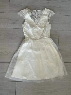 Vit spetsklänning från Nelly - Snygg vit kortklänning från Nelly med omlott upptill och v-ringad spets. Kjolen är i tunn, transparent tyll över ett satinliknande tyg. Klänningen har korta ärmar och dragkedja i ryggen och knappar. Perfekt för dig som vill ha en konfirmationsklänning, skolavslutningnsklänning mm. Jag har använt klänningen 1 gång. Den är i storlek 32 men passar upp till 34. 💕
