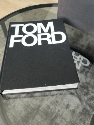 Tom Ford bok med svart omslag - Stilren och exklusiv bok med svart hårt omslag och stora vita bokstäver på framsidan. Perfekt som coffee table book eller för dig som gillar mode och design. Boken är tjock och har en modern känsla, med en matchande skyddskartong.