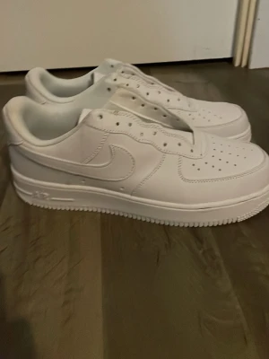 Nike Air Force 1 vita sneakers UTAN SNÖRREN! - Säljer ett par klassiska Nike Air Force 1 sneakers i helvitt läder. Skorna har låg profil, perforerad tå och ikonisk Swoosh på sidan. Perfekta för dig som vill ha en clean och tidlös look. Yttersulan är robust och ger bra grepp.