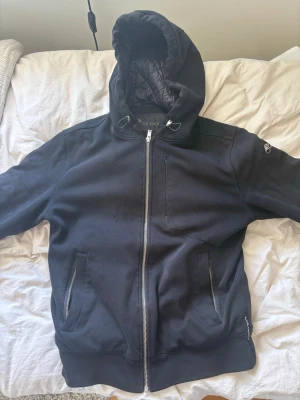 Cardigan från mouseknuckels  - Svart cardigan från Moose Knuckles med hel dragkedja, huva och två fickor framtill. Jackan har ett diskret Moose Knuckles-märke på armen och en stor logga på ryggen. Insidan av huvan är quiltad för extra komfort.Inga defekter eller liknande på jackan, det finns även en nfc tag som hävdar att jackan är äkta. Hör av er vid frågor mvh Carl 