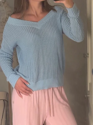 Ljusblå stickad tröja med v-ringning - Ljusblå stickad tröja med bred v-ringning och ribbade muddar. Tröjan har en avslappnad passform och är gjord i ett mjukt stickat material. Perfekt för att skapa en chill och trendig look.