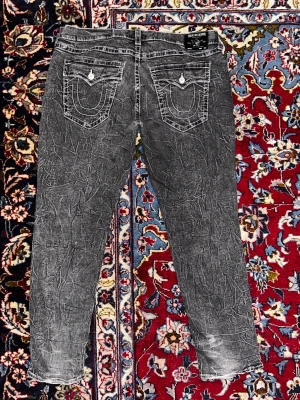 Unika True Religion jeans - Riktigt snygga gråa true religion jeans med unikt wash-pattern. Slitna i hälarna men annars bra skick. Bredd: 58cm. Längd: 116cm
