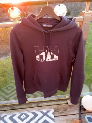 Mörkblå Helly Hansen hoodie - Snygg mörkblå hoodie från Helly Hansen med stor vit logga på bröstet. Klassisk modell med huva och dragsko samt en stor magficka. Perfekt för en chill och sportig stil. Mjuk bomullsblandning som känns skön mot huden. Nästan aldrig använd, Storlek M men sitter mer som en S/XS. Skriv vid minsta fundering🙌🏻🙌🏻