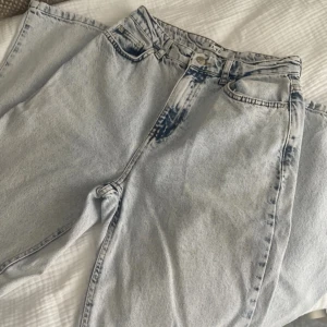 Ljusa baggy jeans från NA-KD - Säljer ett par ljusa baggy jeans från NA-KD med slitna detaljer på bakfickorna. Jeansen har klassisk femficksdesign, hög midja och är gjorda i denim. Perfekt för dig som gillar en avslappnad och trendig look. 