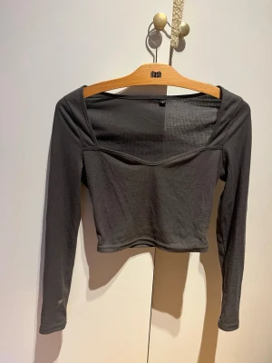 Mörkgrå croppad ribbad topp - Säljer en mörkgrå croppad topp från Flash med ribbad struktur och långärmad design. Toppen har en snygg v-ringad hals och sitter tight. Perfekt för att skapa en cool och trendig look.