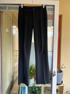 Esprit mörkgrå kostymbyxor storlek 32/34 - Snygga svarta kostymbyxor med klassisk passform och utsvängda ben. Byxorna har hällor för bälte, knapp och dragkedja framtill. Perfekta för dig som vill ha en stilren och tidlös look. Materialet känns mjukt och följsamt.