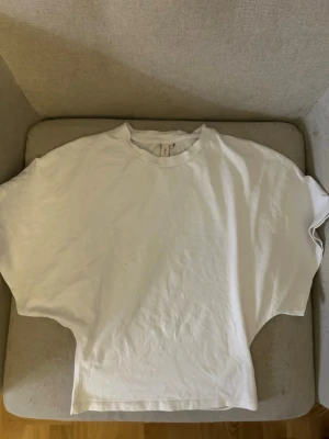 Vit wide sleeve boat neck T-shirt från Nelly - Enkel vit t-shirt med tajt midja från Nelly . T-shirten har korta ärmar och rund halsringning. Perfekt basplagg att styla till olika outfits.