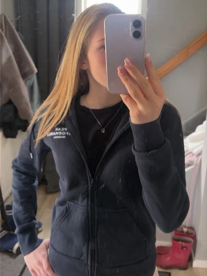 Mörkblå hoodie från Peak Performance - Säljer en mörkblå hoodie från Peak Performance med dragkedja och huva. Modellen har två stora fickor framtill och logotypen tryckt på bröstet. Materialet är mjukt och bekvämt, perfekt för chill dagar. Snygg och enkel design som funkar till det mesta.