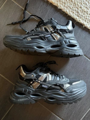 Buffalo svarta chunky sneakers - Buffalo sneakers med chunky sula i svart och silver. Skorna har meshdetaljer, syntetiska paneler och snörning framtill. Tydlig streetwear-vibe med futuristisk design och höga sulor som ger extra attityd till outfiten.