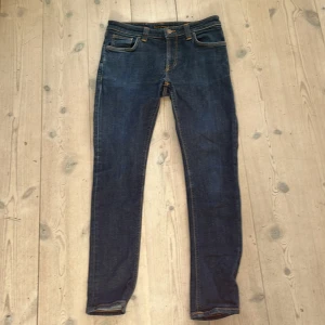 Blå slim fit jeans från Nudie Jeans - Säljer ett par klassiska blå slim fit jeans från Nudie Jeans med fem fickor och snygga kontrastsömmar. look och ikoniska broderade bakfickor. Perfekta för en avslappnad och trendig stil. Pris är ej hugget i sten 