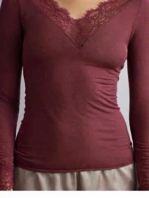 Vinröd topp med spetsdetaljer intimissmi - Snygg vinröd långärmad topp med v-ringning och spetsdetaljer vid halsringning och ärmslut. Figurnära passform och mjukt material som känns skönt mot huden. Perfekt för dig som gillar en feminin och trendig stil.