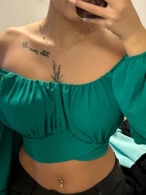 Grön offshoulder croppad topp - Trendig grön offshoulder topp med långa puffärmar och croppad passform. Toppen har en rynkad byst och bred resår under bysten för en snygg siluett. Perfekt för dig som vill sticka ut med en färgstark och modern look. Är i storlek M men passar mig som är XS