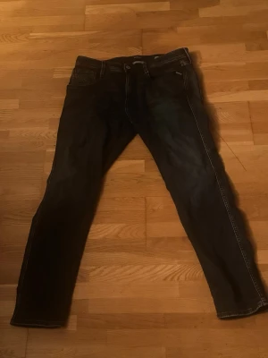 Mörkblå slim fit jeans från Replay - Snygga mörkblå jeans från Replay med slim fit passform och klassisk femficksdesign. Jeansen har vita kontrastsömmar och subtila slitningar framtill. Perfekta för dig som vill ha en stilren och modern look.
