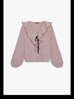 Rutigt blus med volang och knytband - Säljer en så snygg blus från ZARA med rött och vitt rutmönster, volang runt halsen och knytband framtill. Blusen har långa ärmar med resår vid ärmslut och är tillverkad i ett lätt och luftigt material. Kommer tyvärr inte till så mycket användning. Använd 1-2 gånger💓 