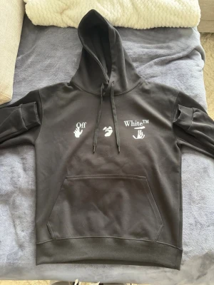 Svart Off-White hoodie med blått tryck - Säljer en svart hoodie från Off-White med vit logga och handmotiv på bröstet samt ett stort blått och vitt grafiskt tryck på ryggen. Hoodien har huva med dragsko och en stor magficka. Perfekt för dig som gillar streetwear och vill sticka ut. Priset kan diskuteras!