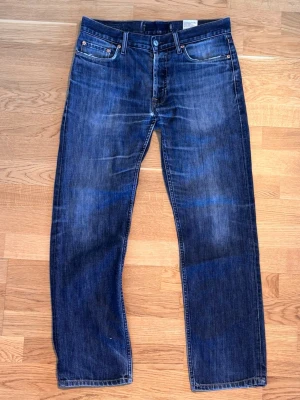 Blå raka jeans från gap - Säljer ett par klassiska blå jeans från Gap med raka ben och fem fickor. Jeansen har en snygg tvätt med subtila slitningar och är tillverkade i bomull. Perfekt för dig som gillar en tidlös och avslappnad stil.