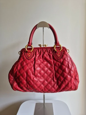 Vinröd quiltad handväska från Marc Jacobs  - Marc Jacobs vinröd quiltad läderväska i mycket fint skick. 100% äkta. Endast små repor på låset samt lätt slitage på ena sidan (se bilder). Väskan har en avtagbar axelrem i kedja. Väldigt efterfrågad modell i vintage-stil "Stam-inspired styles". Det kan hämtas i Solna eller skickas
