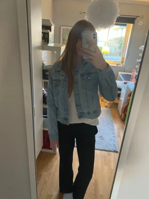 Ljusblå cropped jeansjacka - Trendig ljusblå jeansjacka i croppad modell med klassisk krage och knappar framtill. Två bröstfickor med lock och knappdetaljer. Perfekt nu till våren och sommaren när det blir varmt och man vill klä sig enkelt.