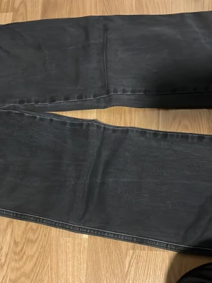 Svarta raka jeans med fickdetalj - Säljer ett par svarta jeans med raka ben och snygg fickdetalj bak med knapp. Jeansen har klassisk femficksmodell och är tillverkade i denim med lätt tvättad look. Perfekta för en avslappnad och trendig stil.