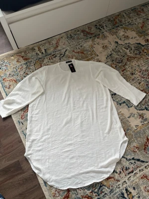 Vit klänning med trekvartsärm - En stilren vit klänning från Bik Bok med trekvartsärmar och rundad nederkant. Klänningen har en enkel och avslappnad passform, perfekt för en trendig och bekväm look. Tillverkad i ett mjukt material som känns skönt mot huden.