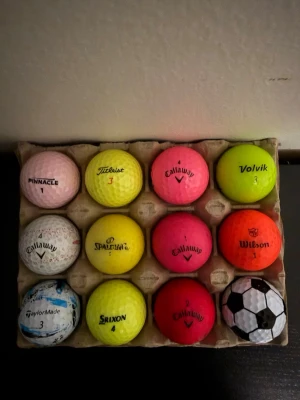 Färgglada golfbollar mixade märken - Säljer ett set med 12 golfbollar i olika färger och märken. Bollarna är rosa, gula, vita, orange, röda och en med fotbollsmönster. Perfekt för dig som vill ha variation på golfbanan eller synas extra mycket.