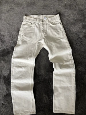 Vita raka jeans med hög midja - Säljer ett par vita jeans med rak passform och hög midja. Klassisk femficksmodell med knappgylf och bälteshällor. Perfekta till en clean och stilren look. Materialet är kraftig denim i bomull.