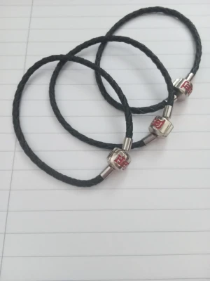 Svarta armband  - Säljer tre armband med svart flätad rem och metallpärlor med röd text 'Hej'. Säljer alla tre för 60 kr, annars en för 20 kr. Notera att de är små i storleken.