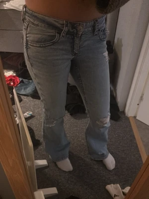 Ljusblå bootcut jeans med slitningar - Säljer ett par ljusblå, lågmidjade bootcut jeans från Gina tricot. De har mörkröda sömmar på sidorna. Passar xs