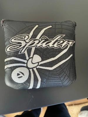 Svart Spider fodral med spindelmotiv taylormade golfputterheadcovet - Snyggt svart fodral i konstläder med broderad spindel och texten 'Spider' på framsidan. Fodralet har kardborrestängning och mjukt, fluffigt innerfoder. . Unik design med spindelnätmönster från taylormade