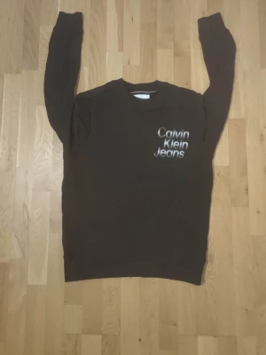 Svart sweatshirt från Calvin Klein Jeans - Svart sweatshirt från Calvin Klein Jeans med vit logga tryckt på bröstet. Klassisk rund halsringning och långa ärmar. Perfekt för en avslappnad och stilren look. Tillverkad i mjukt material för extra komfort.