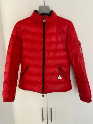 Röd Moncler jacka dam - Säljer denna röda moncler jacka i dam storlek. Den har storlek 2. Jackan är i rätt bra skick förutom stora lappen på insidan. Den gick tyvärr bort under kemtvätt. Frågor eller funderingar är det bara å säga till!