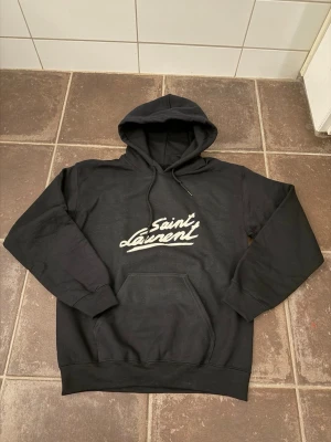Saint Laurent hoodie  - Riktigt fet och eftertraktad hoodie med saint Laurent loggan i storlek S. Väldigt bra skick! längd cirka 62cm, bredd cirka 48cm. Obs: Jag är lite osäker på äktheten då lappen i nacken saknas, därför säljs den billigare (700 kr, nypris ca 3000 kr). Tveka inte att höra av dig vid frågor eller funderingar!