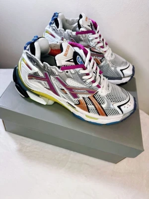 ASICS Gel-Kayano 14 sneakers - Färgstarka ASICS Gel-Kayano 14 sneakers med mesh och syntetmaterial. Skorna har silver, lila, orange och gula detaljer, vit bas och blå inslag på sulan. De har en chunky design med coola kontraster och klassisk ASICS-logga på sidan.