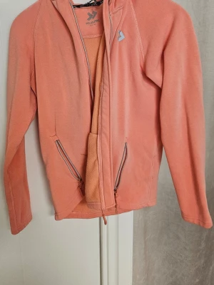 Korallrosa fleecejacka från Everest - Mysig korallrosa fleecejacka från Everest med dragkedja framtill och två fickor med dragkedja. Jackan har lång ärm och en enkel, sportig design som passar perfekt till lager-på-lager-stil.
