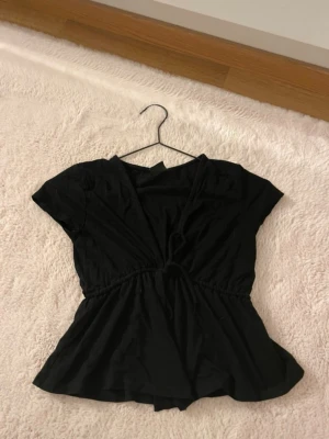 Topp med knyt från Gina Tricot - Snygg svart omlottopp från Gina Tricot med korta armar och knyt i midjan. Toppen faller fint och är i skönt material. Perfekt att styla båda till vardag och fest. Endast använd ett fåtal gånger!