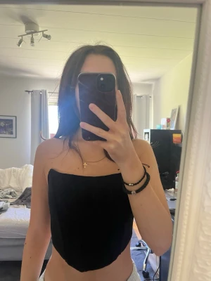 Svart tubtopp i bandeau-modell - Svart tubtopp i bandeau-stil med enkel och stilren design. Toppen är ärmlös och har en rak nederkant.