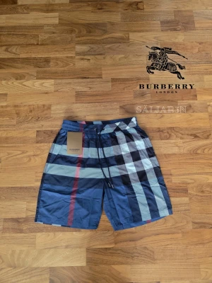 Burberry Shorts - 🩳 Burberry Shorts – Storlek M 🩳 Stilrena Burberry shorts med klassiskt rutmönster, perfekta för sommar, strand eller avslappnad vardag. Elastisk midja med justerbar dragsko ger bekväm passform. Tillverkade i lätt och slitstarkt material med mjuk känsla mot huden. Praktiska fickor för småsaker och Burberry-logga på detaljerna ger en lyxig finish. Shortsarna är i nyskick. 📦 Snabb leverans – Kontakta för frågor!