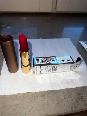 Lancôme rött läppstift 888 Kind of Sexy - Snyggt rött läppstift från Lancôme i nyansen 888 Kind of Sexy. Kommer i en lyxig guldig hylsa med brunt lock och vacker rosdetalj på toppen. Förpackningen är elegant och stilren, perfekt för dig som vill ha en klassisk röd färg på läpparna.