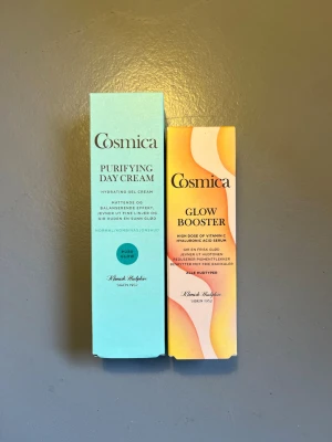 Cosmica dagkräm & glow booster - Två produkter från Cosmica: Purifying Day Cream i ljusblå förpackning (50 ml) och Glow Booster i färgglad förpackning (30 ml). Dagkrämen är en återfuktande gelkräm och glow boostern är ett serum med vitamin C och hyaluronsyra.