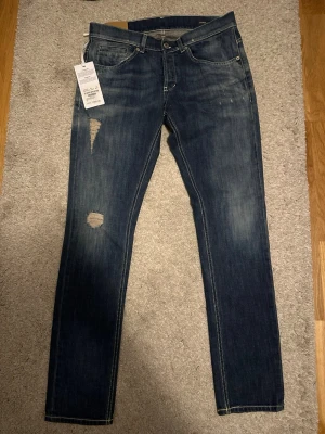 Dondup George - 2800kr Nya med tags. Säljer ett par mörkblå jeans från Nudie Jeans med slitningar och hål på vänster lår. Klassisk femficksmodell med kontrastsömmar och smal passform. Jeansen har en snygg tvättad look och är tillverkade i bomull. Perfekta för en avslappnad stil.