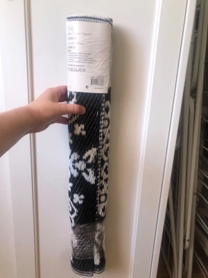 Ny Svartvit plastmatta mått:60 /90,  Janina - Säljer en oanvänd svartvit plastmatta, modell Janna. Mattan har ett grafiskt mönster i svart och vitt och är tillverkad av 100% polypropen. Perfekt för både inomhus och utomhusbruk tack vare det tåliga materialet.
