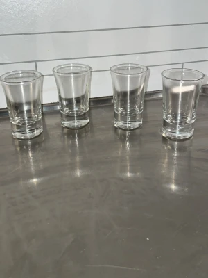 Fyra genomskinliga shotglas - Säljer fyra klassiska shotglas i genomskinligt glas. Glasen har en rak form med lätt utåtböjd kant upptill och tjock botten. Perfekta till festen eller samlingen av barprylar.
