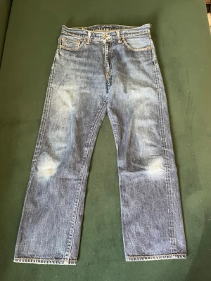 SKIT FETA MOMONTARO  - Klassiska blå MOMONTARO jeans med raka ben och fem fickor. Jeansen har en snygg tvätt med slitningar på knän och lår, samt kontrastsömmar och läderpatch bak i midjan. Tillverkade i slitstark denim, perfekt för en avslappnad och trendig look.
