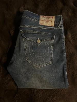 True Religion Ricky Relaxed Straight Jeans W36 - Snygga True Religion bootcut jeans i modellen Ricky Relaxed Straight. Storlek W36. Klassisk mörkblå tvätt med vita stygn. Mycket skick och en riktigt stilren modell som sitter bra och är lätt att matcha.