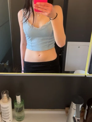 Ljusblå ribbad linnetopp med spets - Söt ljusblå linnetopp med tunna dubbel axelband och ribbad struktur. Toppen har v-ringning och dekorativ spetskant längs urringningen för en extra feminin touch. Perfekt att styla med jeans eller kjol.