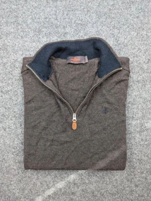  Halvzip tröja i 100% merino ull från Morris  - Mörkbrun stickad tröja från Morris med halvzip och hög krage i mörkblått. Tröjan har en liten broderad logga på bröstet och detaljer i läder på dragkedjan. Perfekt för lager på lager och en stilren look. 100% MERINOULL