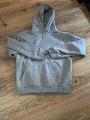 Grå hoodie från Weekday - Klassisk grå hoodie från Weekday med stor känguruficka framtill och huva. Tillverkad i mjukt bomullsmaterial som känns skönt mot huden. Perfekt för en avslappnad och stilren look. Passar till det mesta och är enkel att matcha.